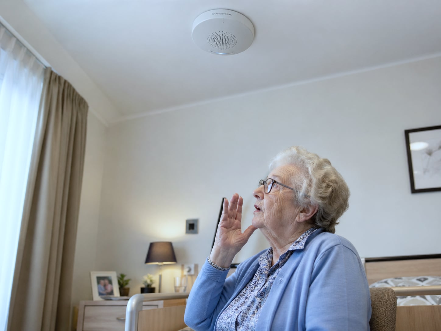 Soignante en polo bleu marine prenant un appel d'interphonie sur smartphone Android professionnel à l'entrée d'une maison de repos belge, visiteur identifié à la porte, installation Healthcall
